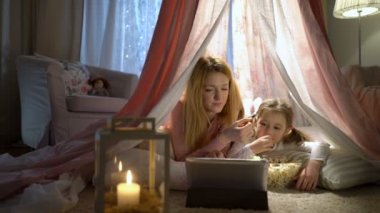 Küçük kız ve annesi odasında çadırda online çizgi film izlerken zevk