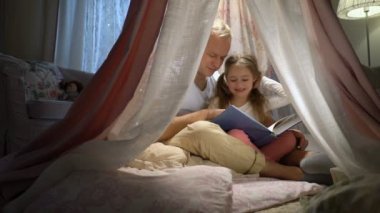 Mutlu aile anne ve küçük kızı çadırda evde kitap okurken