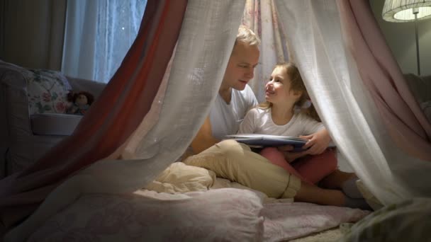 幸せな家族の母と彼女の小さな娘が家でテントの中で本を読んで — ストック動画