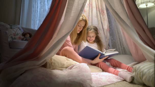 Gelukkige familie moeder en haar dochtertje lezen van een boek in een tent thuis — Stockvideo