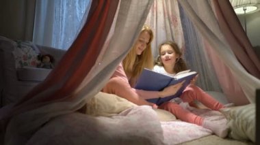 Mutlu aile anne ve küçük kızı çadırda evde kitap okurken