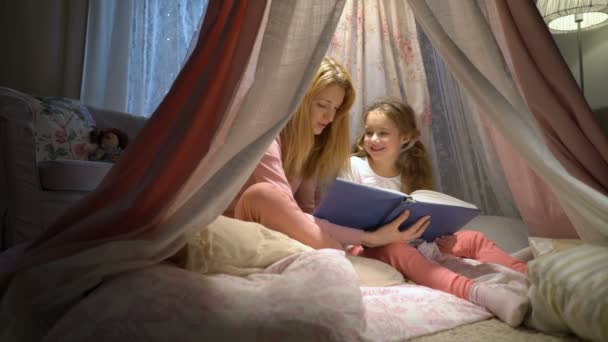 Glückliche Familienmutter und ihre kleine Tochter beim Lesen eines Buches im heimischen Zelt — Stockvideo