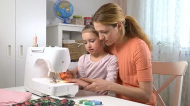 Anne evde kreşte bir dikiş makinesi kullanarak dikiş küçük kızı öğretiyor