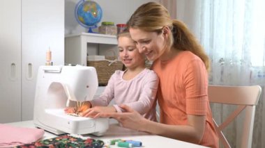 Anne evde kreşte bir dikiş makinesi kullanarak dikiş küçük kızı öğretiyor