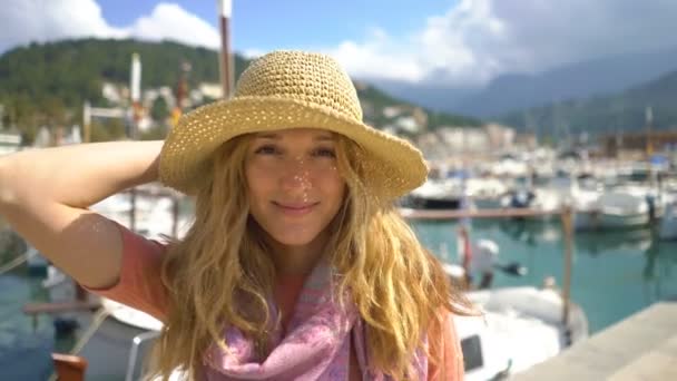 Saman şapkalı genç kadının deniz kıyısı arka planıyla kameraya gülümseyen portresi. — Stok video