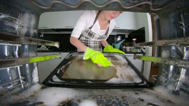 Mulher usando luvas de borracha verde limpando um forno sujo na cozinha usando um detergente . — Vídeo de Stock