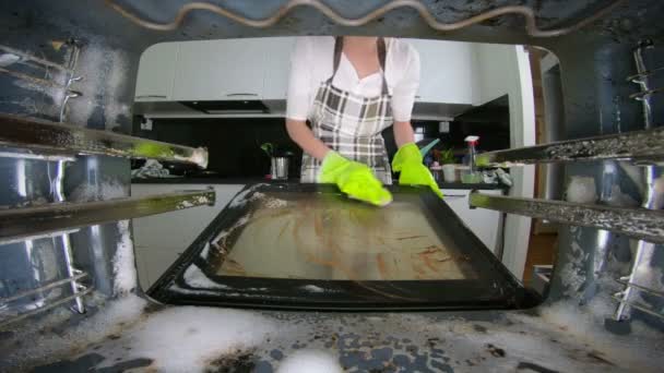 Mujer con guantes de goma verde limpiando un horno sucio en la cocina usando un detergente . — Vídeo de stock