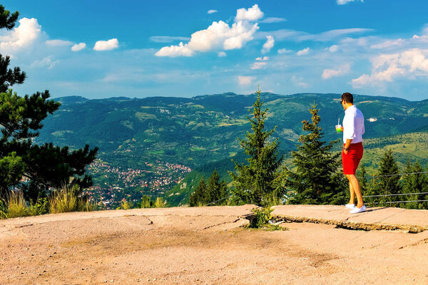 A young guy looks down at the valley and the mountains standing on a high point. Bosnia and Herzegovina, Sarajevo, August 2018
