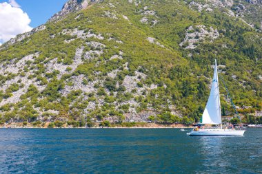 İnanılmaz parlak deniz manzarası. Yeşil ormanlık dağlar ve mavi deniz, mavi gökyüzü ve beyaz bulutlar ve dalgaları aracılığıyla dağlar arasında yelken yat görünümünü. Boka Kotorska Bay, Karadağ