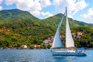 İnanılmaz parlak deniz manzarası. Yeşil ormanlık dağlar ve mavi deniz, mavi gökyüzü ve beyaz bulutlar ve dalgaları aracılığıyla dağlar arasında yelken yat görünümünü. Boka Kotorska Bay, Karadağ