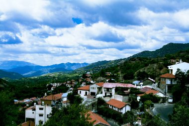 Manzara, dağların, ormanın ve kırmızı çatılı küçük bir köyün manzarasını sunmaktadır. Kıbrıs, Troodos