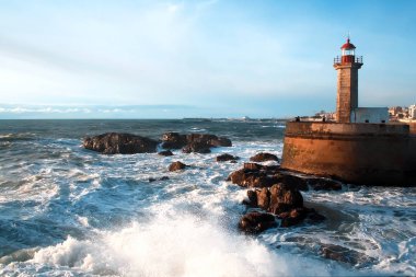 Atlantik Okyanusu 'nun dalgaları gün batımında deniz fenerinin yanındaki kayalara çarpar.