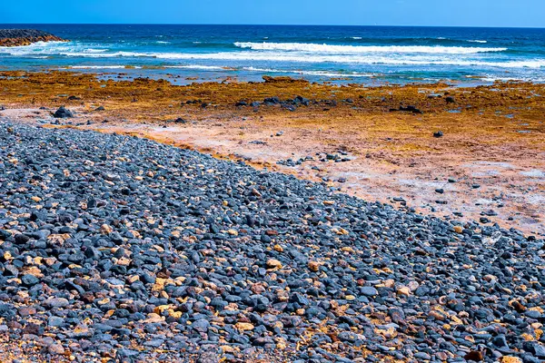 Små stenar på en svart strand, i bakgrunden är Akean vågor och en surfare — Stockfoto