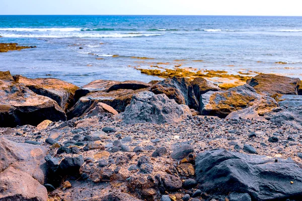 De petites pierres sur une plage noire, en arrière-plan sont des vagues akéennes et un surfeur — Photo