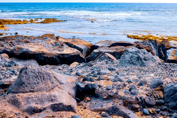 Pequeñas piedras en una playa negra, en el fondo son olas akean y un surfista — Foto de Stock