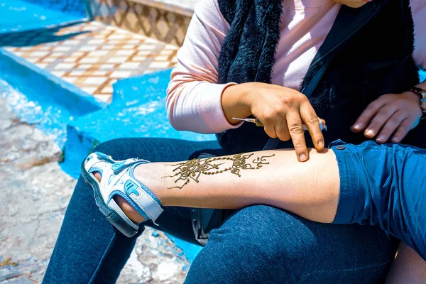 Fas'ın Marakeş sokaklarında kadınların bacağına kına dövmesi uygulayan sanatçı — Stok fotoğraf