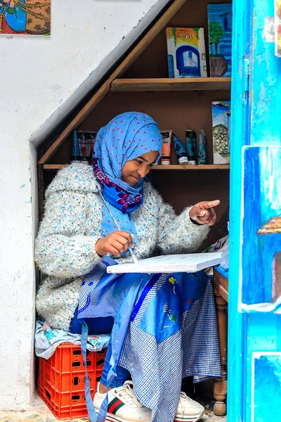 Uma bela menina marroquina, uma muçulmana, artista de rua pinta um quadro com um pincel em uma pequena oficina — Fotografia de Stock