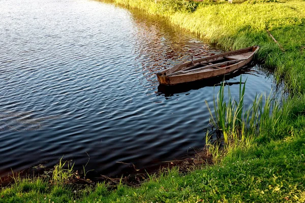 A small wooden rowing boat with a broken bottom on a calm lake near the shore. — Stock Photo, Image