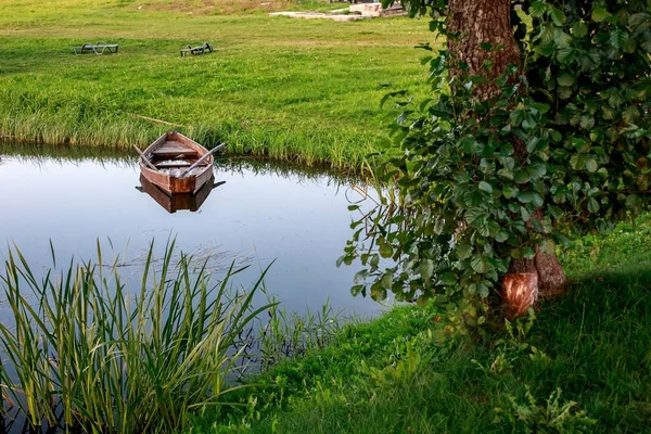 Um pequeno barco a remo de madeira com um fundo quebrado em um lago calmo perto da costa . — Fotografia de Stock