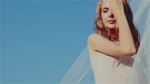 阳光灿烂的一天 一个漂亮的金发无忧无虑的女孩站在田野里 在风吹来的白色透明织物的衬托下 在风中理直了头发 慢动作 — 图库视频影像