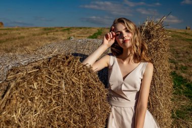 Güneşli bir günde durup poz veren sarışın bir genç kızın portresi samanlıkların ve mavi gökyüzünün arka planında