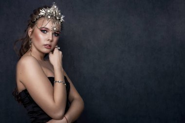 Gri bir arka planda taç ve kostüm takan sarışın güzel bir kadının portresi. Güzellik konsepti