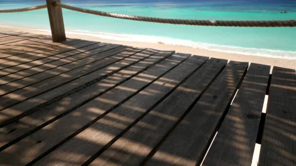 Тени пальмовых листьев на деревянной палубе с размытым пляжем на заднем плане. Разрешение 4K — стоковое видео