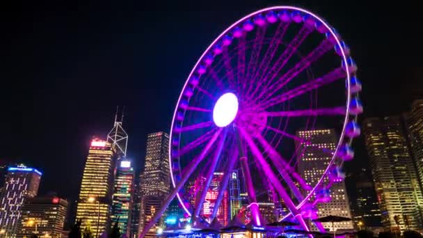 Hong Kong - Glowing night cityscape з колесом і хмарочосами на задньому плані. Збільшення часового пропуску 4K. — стокове відео