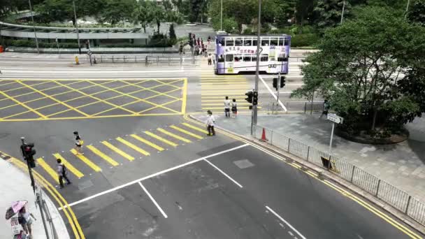 HONG KONG - Gente cruzando la calle en el centro de la ciudad con el tráfico y tranvías de dos pisos que pasan. Velocidad de resolución 4K . — Vídeo de stock