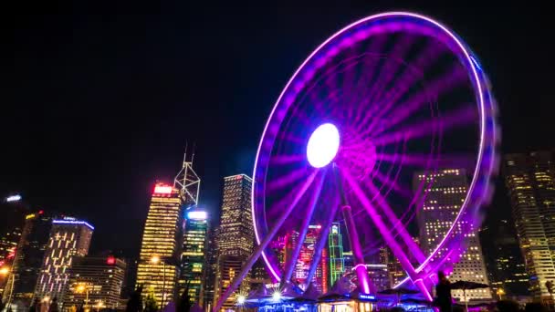 Hong Kong - Paisaje nocturno brillante con noria y rascacielos en el fondo. Caducidad de resolución 4K. Velocidad de obturación larga . — Vídeos de Stock