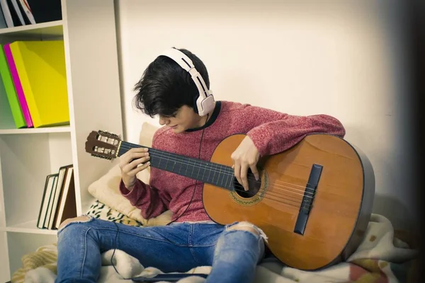 young playing guitar with headphones at home