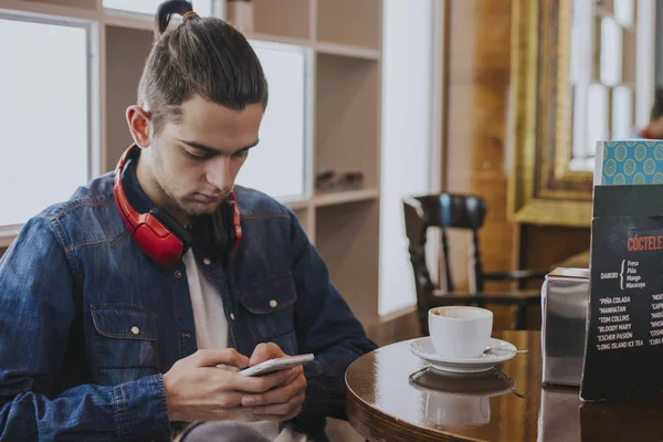 young man with headphones and phone in the cafeteria