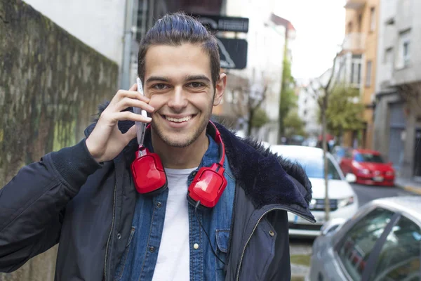 青年用耳机走在街上用手机 — 图库照片