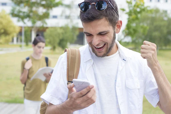 students with mobile phone or smartphone celebrating success