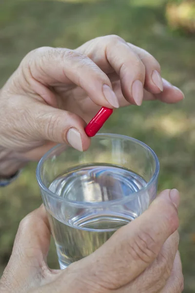 older woman hand with pills and a glass of water