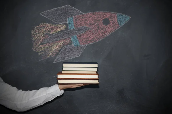 hand with books and drawing of rocket or spacecraft