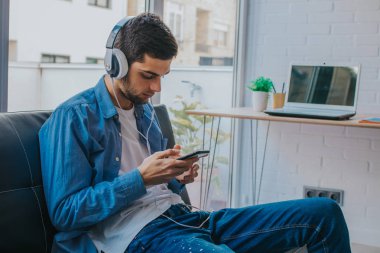 evde cep telefonu ve kulaklık ile genç adam veya genç