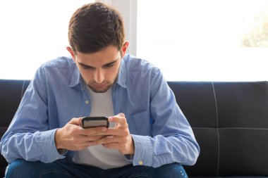 Evde cep telefonu olan genç bir adam.