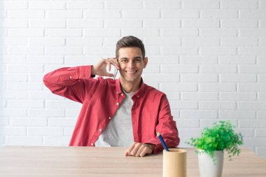 Evde ya da ofiste cep telefonu olan genç bir adam.