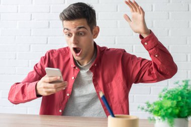 şaşırmış genç adam cep telefonunu izliyor.