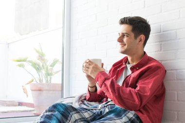 Genç adam kahvaltı yapıyor ya da evde kahve içiyor.