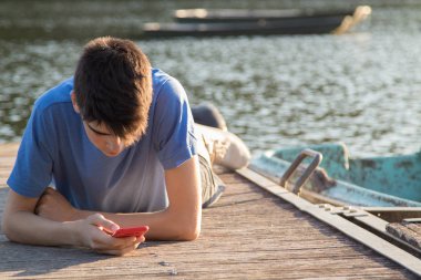 Gün batımında iskelede cep telefonu olan genç bir adam.