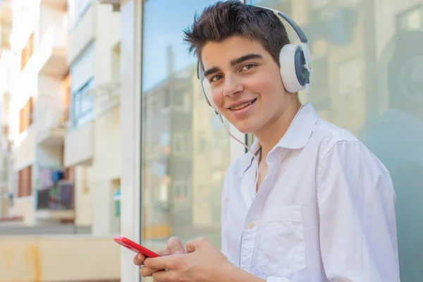 young man with phone and headphones listening to music outdoors in the city