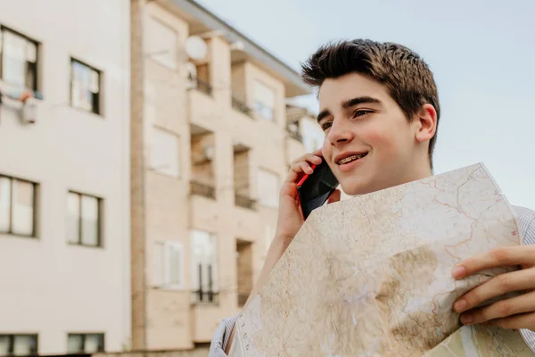 trendy young man with map and mobile phone on city street