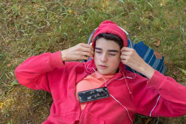 Cep telefonu ve kulaklıklı genç adam sahada yatıyor.