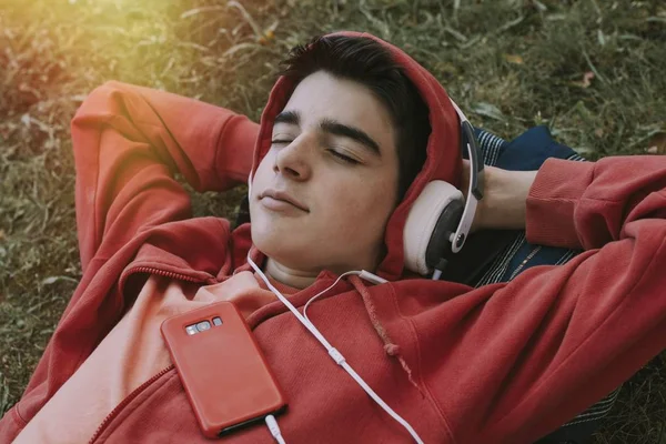 年轻的少男 手持耳机和手机躺在田里 — 图库照片