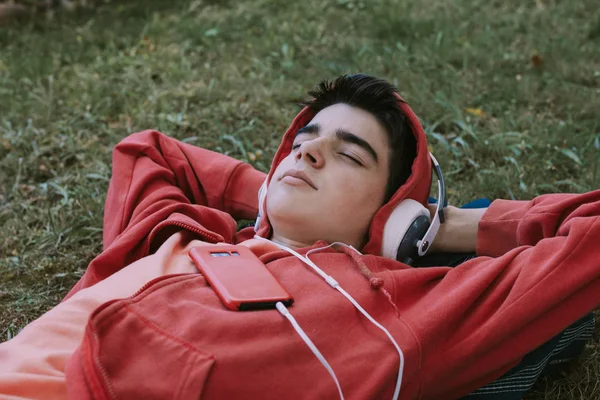 young teenage male with headphones and phone lying in the field