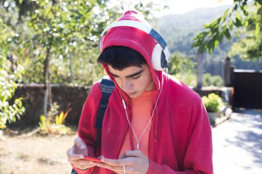 Dışarıda cep telefonu ve kulaklığı olan genç bir adam veya öğrenci.