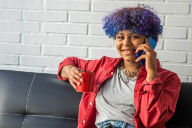 Cep telefonu ve bir fincan kahveyle gülümseyen genç kız.