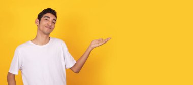 Genç bir adam beyaz tişörtle izole edilmiş bir arkaplanı işaret ediyor.